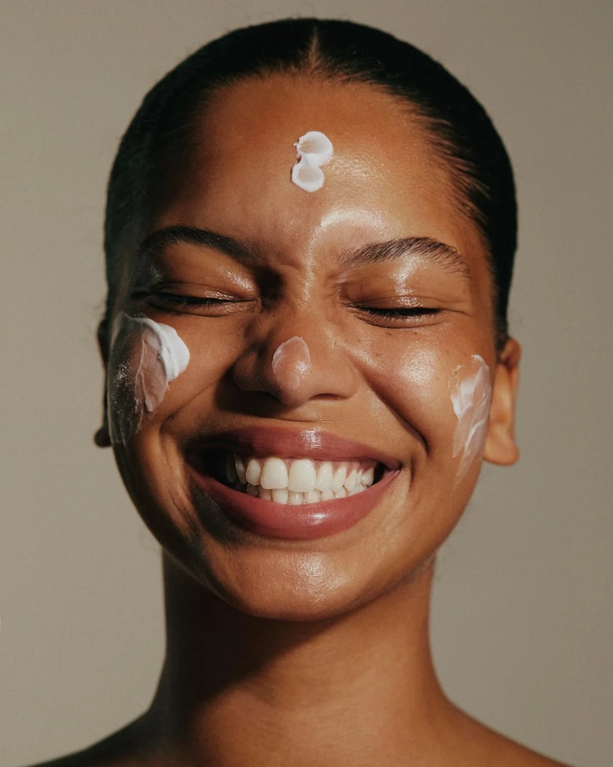 Femme souriante, yeux fermés, crème sur le front et les joues